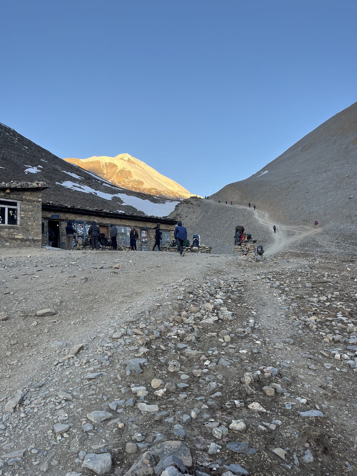 Trekkers walking past a lodge as first light gilds a peak