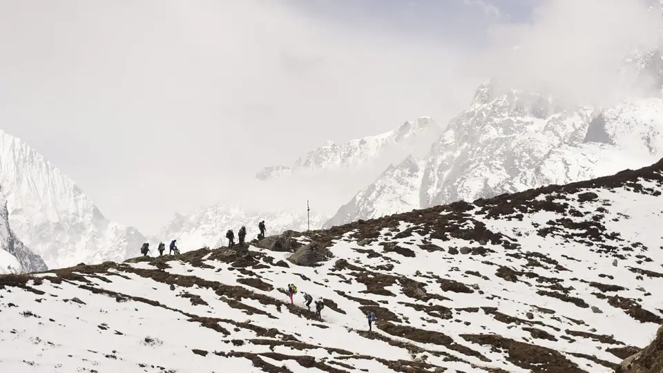 Line of trekkers walking a snowy ridge in the distance