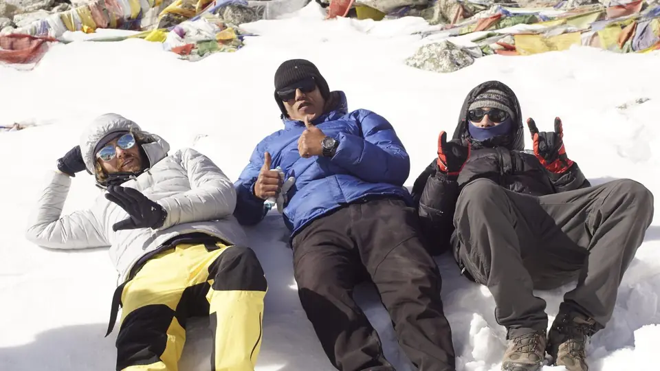 Three trekkers resting in the snow surrounded by prayer flags