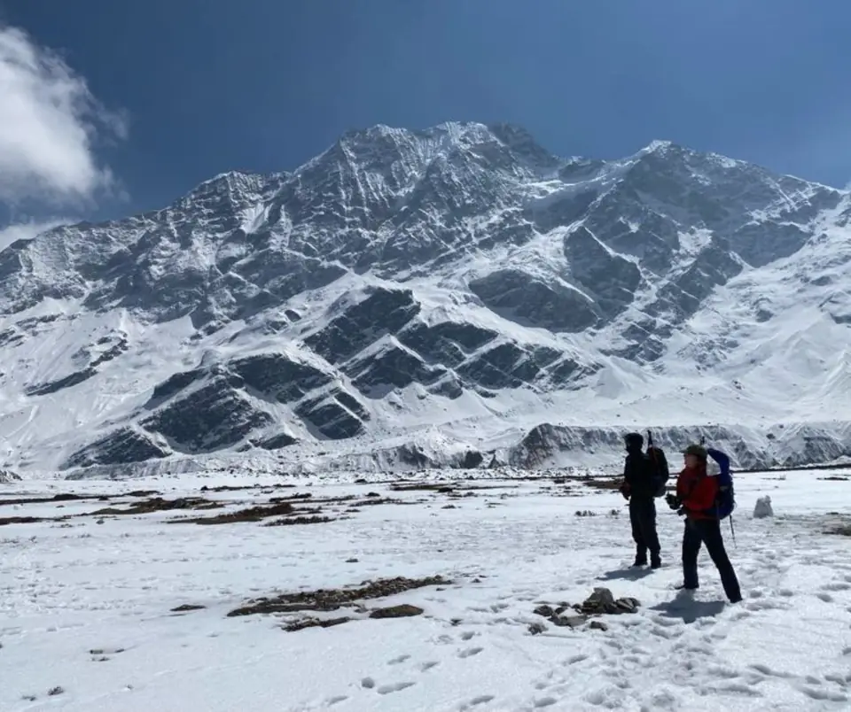 Two trekkers on a snowy ridge with a panorama of peaks