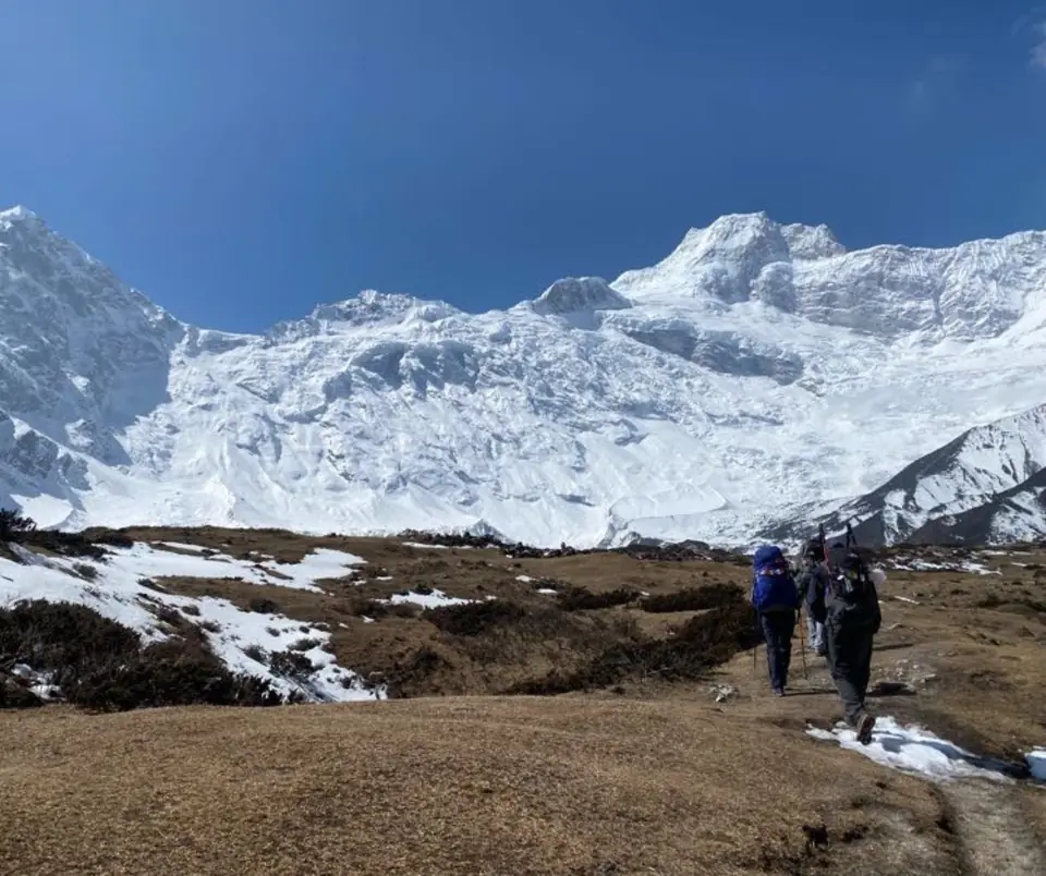 Trekkers walking a dusty trail toward snow slopes
