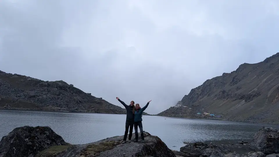 Two trekkers with arms raised beside a Gosaikunda lake