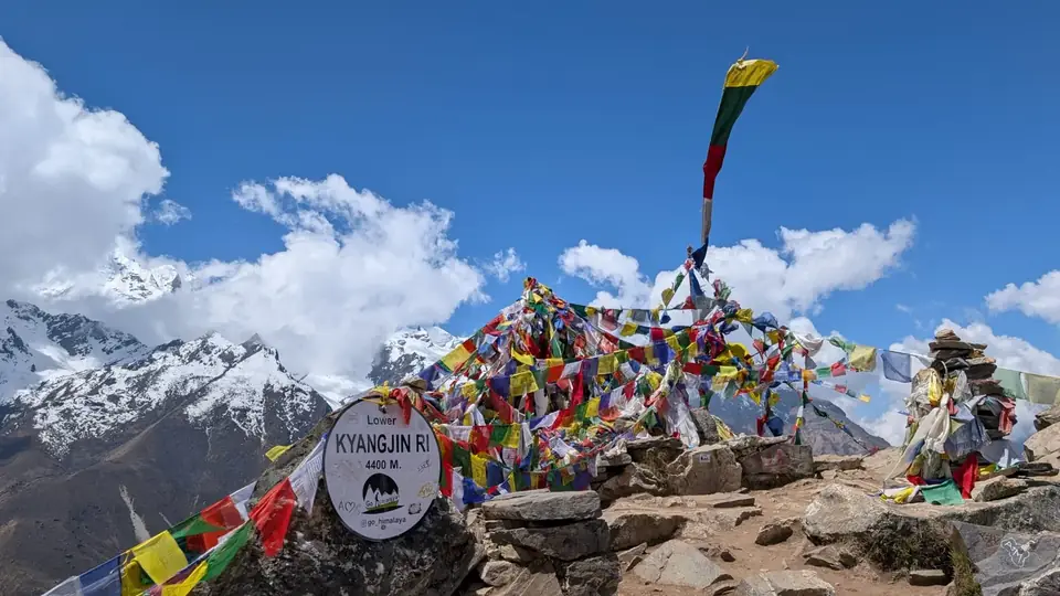 Colourful prayer flags on the Kyanjin Ri summit with snow peaks and blue sky