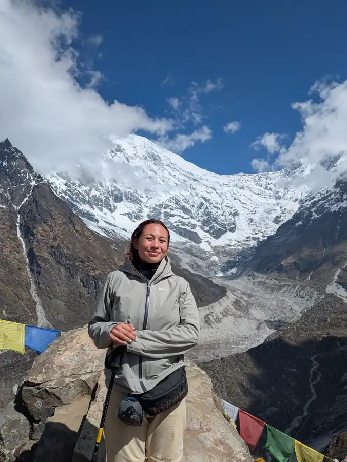 A trekker resting below a towering snow peak hung with prayer flags