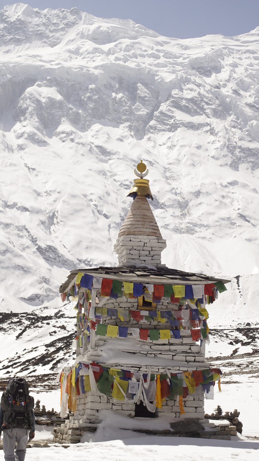Stone chorten hung with colourful prayer flags below snow-covered slopes