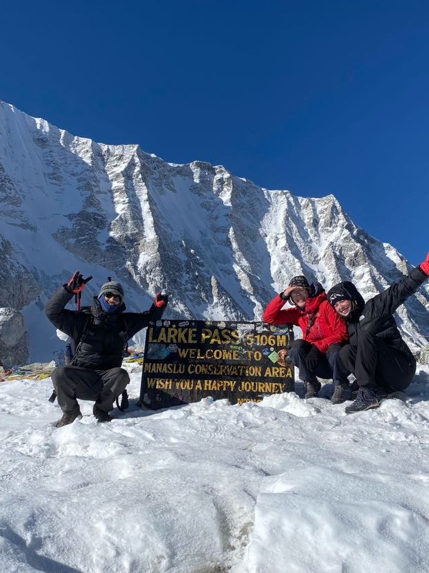 Trekkers celebrating with arms raised beside the Larke Pass sign